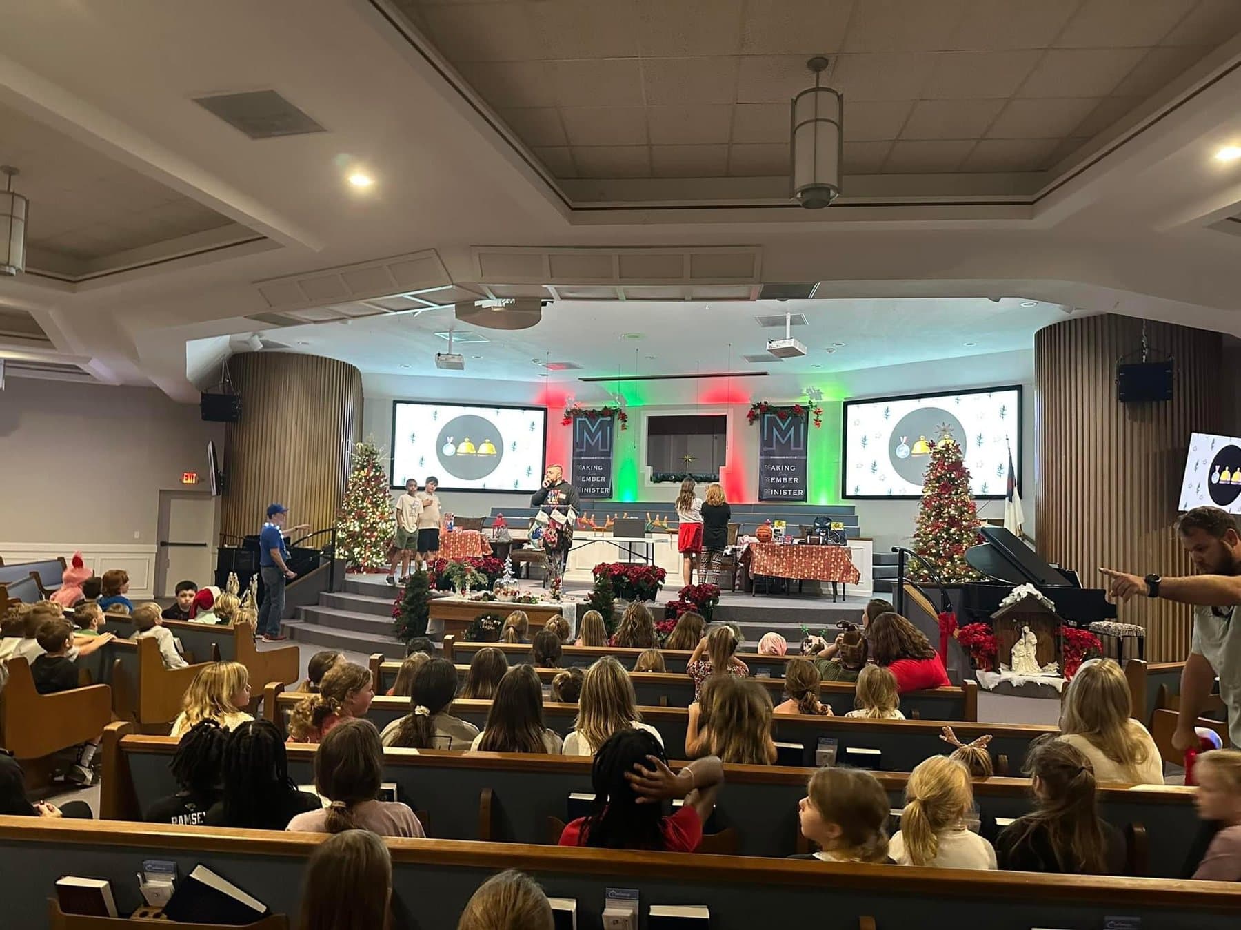 A packed Christmas service at Calvary, with two lit trees flanking the platform and poinsettias along the steps