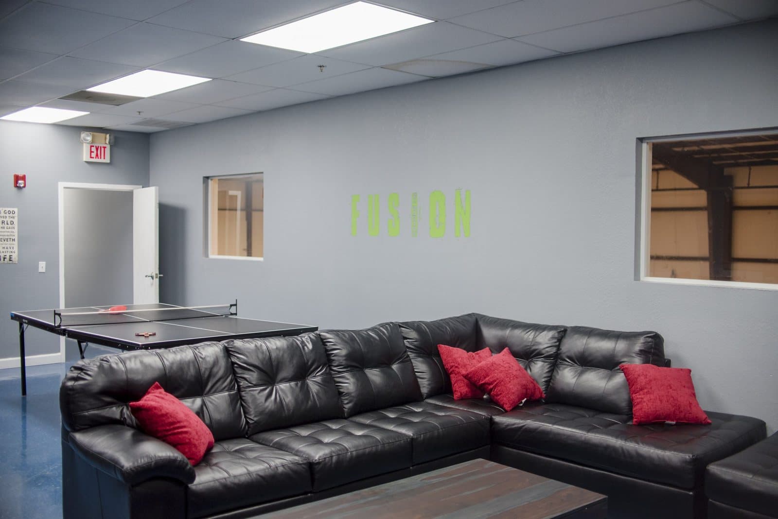 The FUSION student lounge — a black sectional couch with red pillows and a ping-pong table against a grey wall
