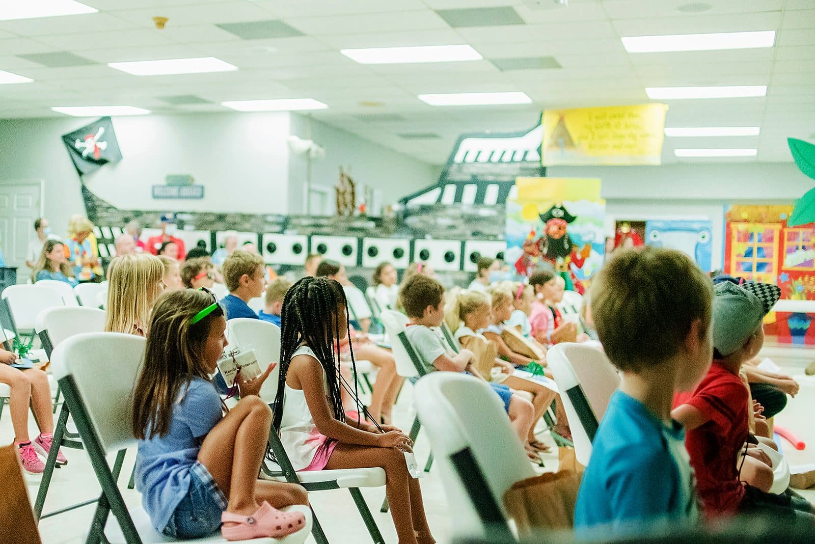 Children on folding chairs in a decorated classroom during Kids J.A.M. on a Wednesday night