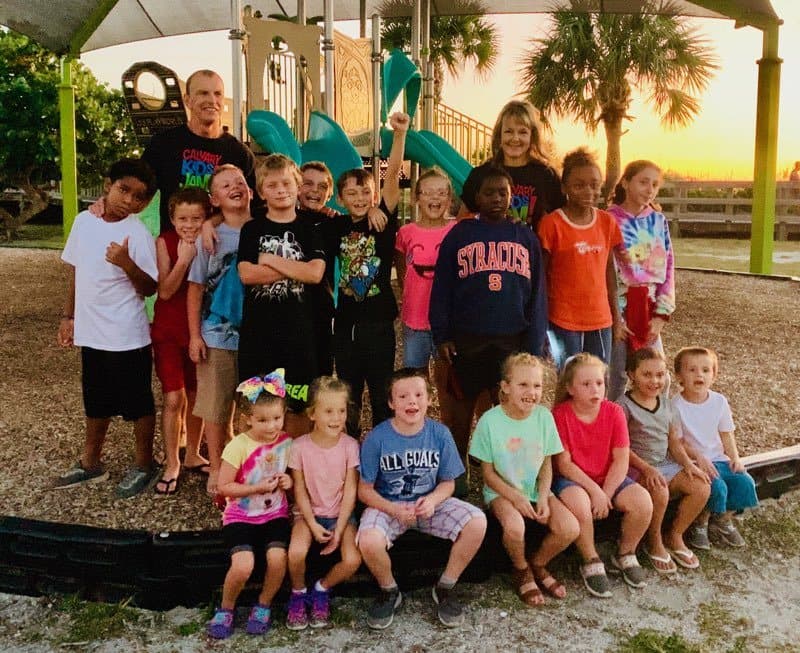 A group of children gathered on the church playground under palm trees at the end of the day