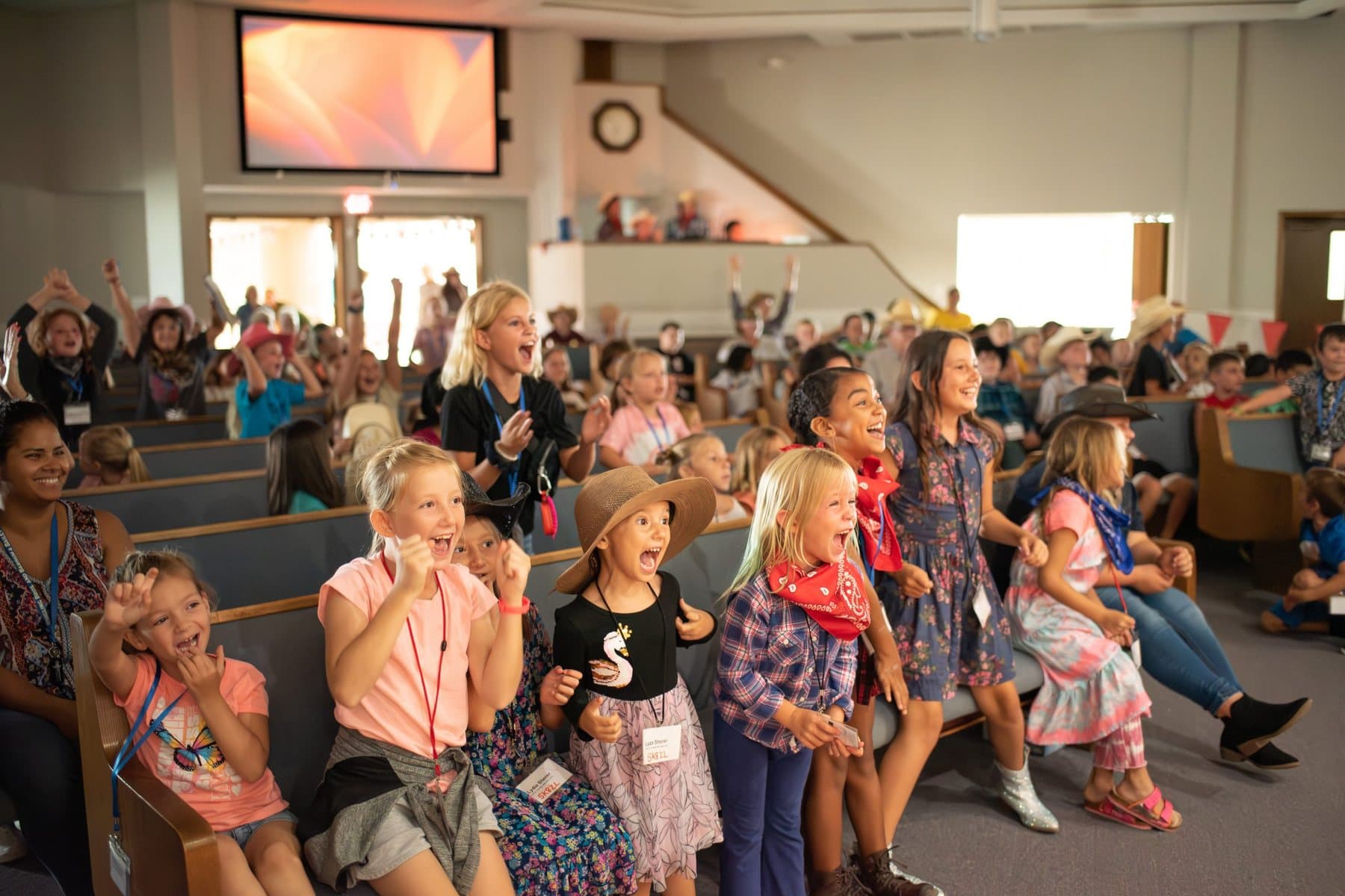 A room full of children and their leaders singing with hands raised during Vacation Bible School